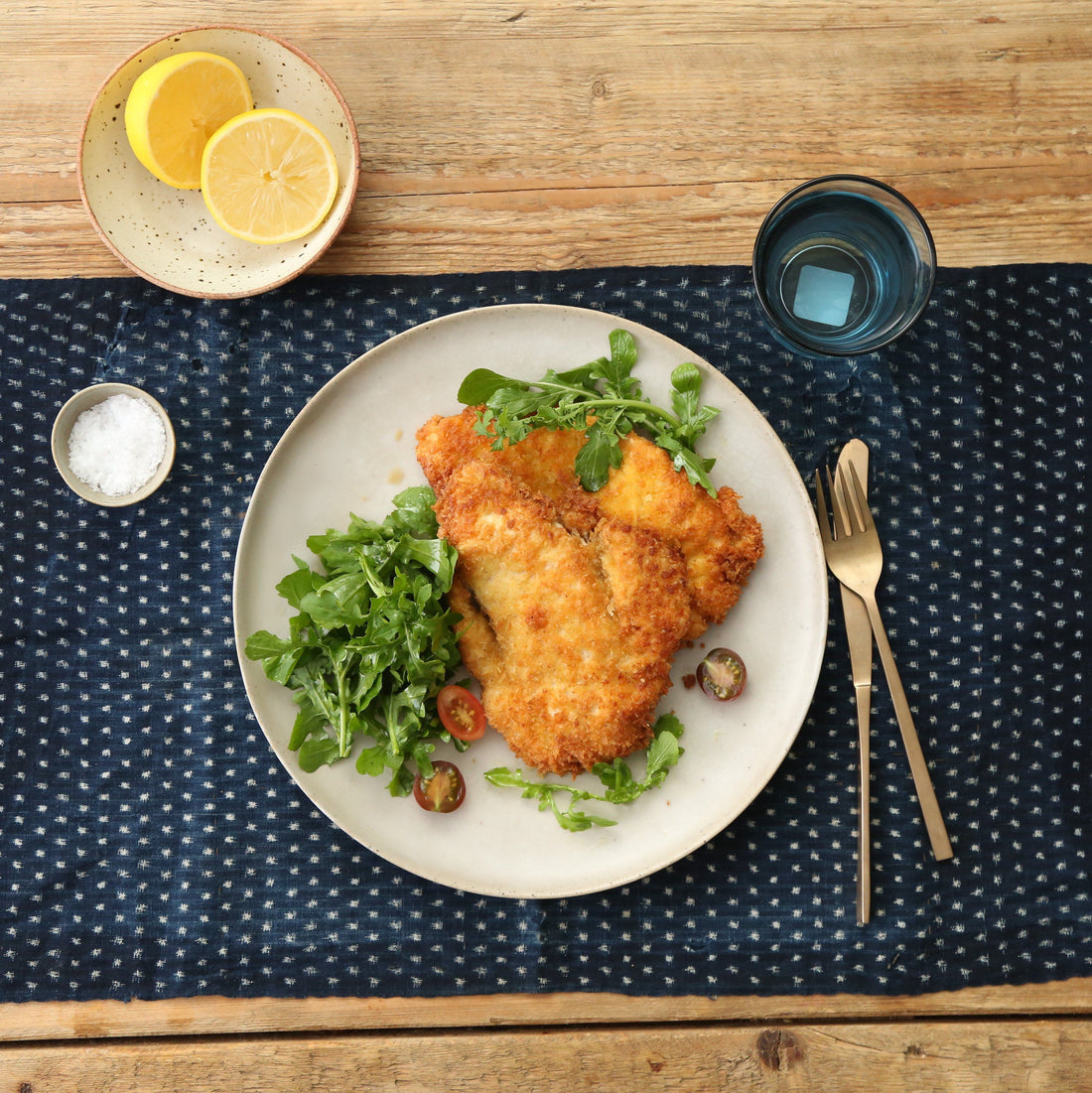 Cooked chicken schnitzel on a plate with a salad and cutlery.
