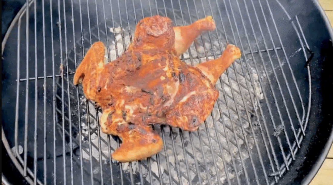 A spatchcock chicken on a black, round Weber charcoal grill.
