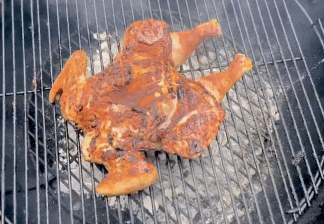 A spatchcock chicken on a black, round Weber charcoal grill.