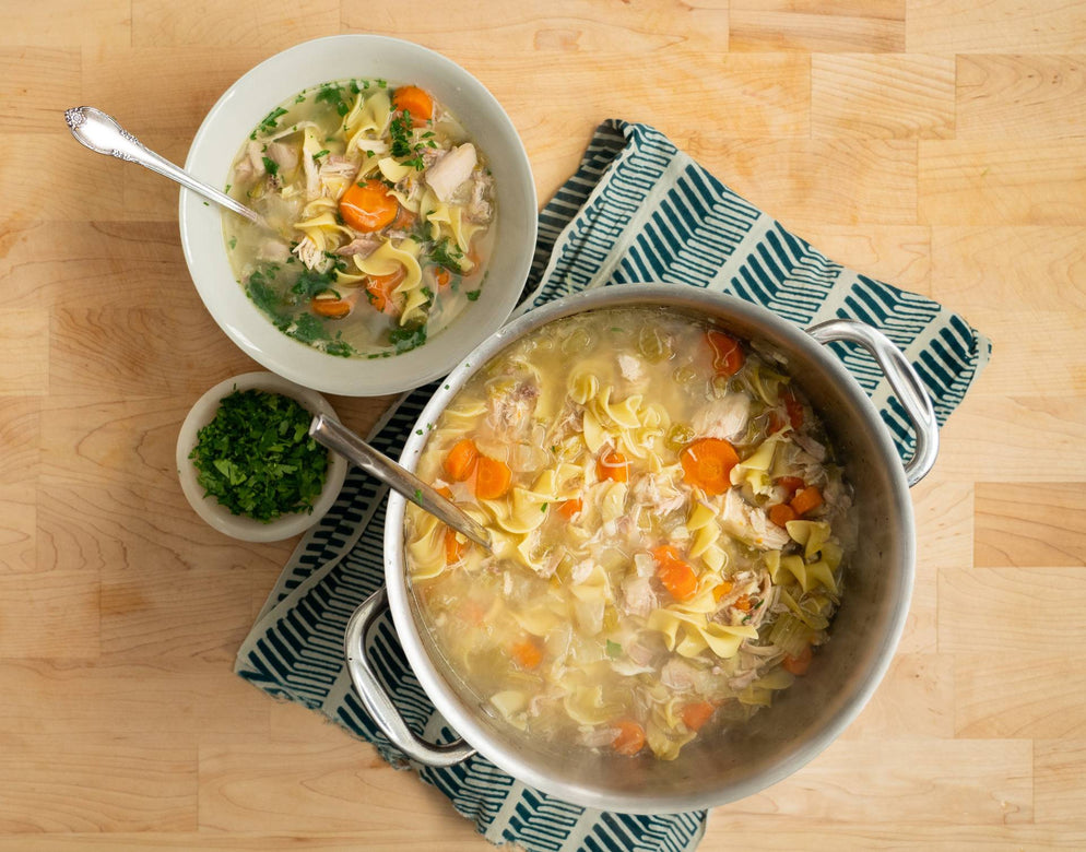 A pot and bowl of pasture-raised chicken noodle soup sitting on a table ready to eat.