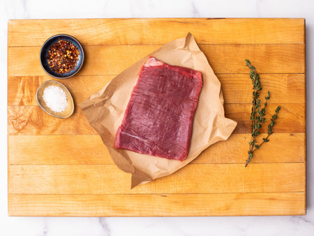 Flank steak on a cutting board next to seasoning.