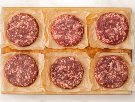 Uncooked 85% lean burger patties on a cutting board.