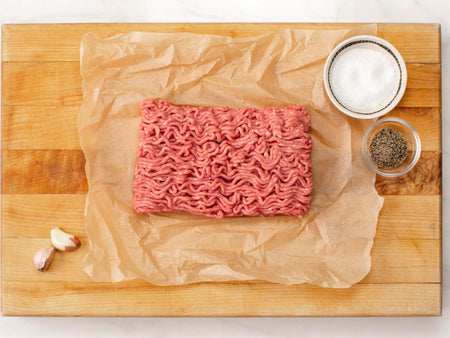 Uncooked ground beef on a cutting board next to salt and pepper.